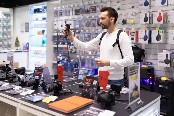 민스크, 벨라루스 - 2021 년 9 월 27 일: 흰색 스웨트 셔츠를 입은 머리를 한 남자의 사진 이 쇼핑 센터의 전자 상가에서 카메라를 선택 한다. 가게의 개념 — 스톡 사진