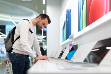 Minsk, Belarus - 27 Kasım 2021: Beyaz kazaklı, sakallı, yetişkin, yakışıklı bir esmer adamın iş için bir bilgisayar bilgisayarı seçmesi ve alışveriş merkezindeki bir elektronik mağazasında ders çalışması