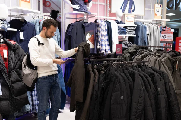 Minsk, Bielorussia - 27 novembre 2021: Un bel brunetto adulto sceglie una giacca calda in un negozio di abbigliamento in un centro commerciale. Capispalla e shopping — Foto Stock