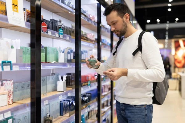 Minszk, Fehéroroszország - nov 27, 2021: Fénykép egy felnőtt jóképű barna férfi borosta fehér pulóver választ parfüm és adekolon egy parfüm boltban egy bevásárlóközpont — Stock Fotó