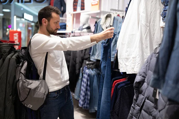 Homem morena bonito adulto escolhe camisa e camiseta em uma loja de roupas em um shopping center. Compras — Fotografia de Stock