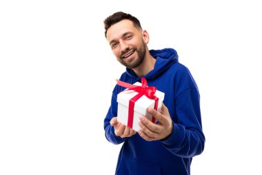 Beyaz arka planda mavi kapüşonlu bir adam beyaz bir kutuda elinde kırmızı bir kurdeleyle bir hediye tutuyor.