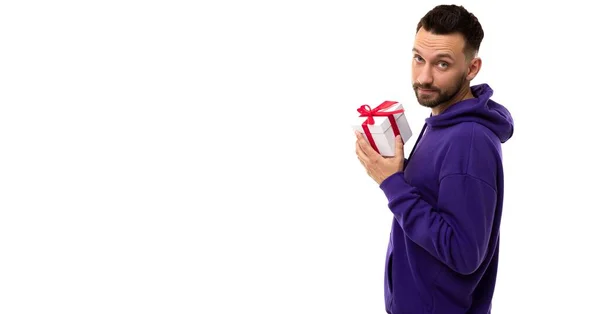 Un joven con una sudadera azul sosteniendo una caja de regalo con un lazo rojo —  Fotos de Stock