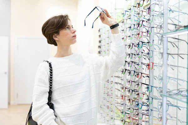 Mujer joven cerca de pie de gafas en el salón de oftalmología — Foto de Stock