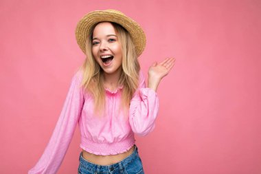Çekici, gülümseyen hippi sarışın kadının portresi. Pembe hasır bluz ve hasır şapka. Stüdyoda pembe duvarın yanında yalnız poz veren kaygısız seksi kadın. Doğal olarak pozitif model.