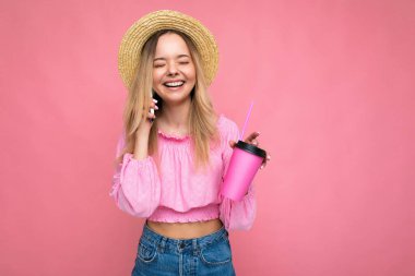 Pembe arka planda kahve içerken cep telefonuyla konuşan mutlu genç bir kadın.