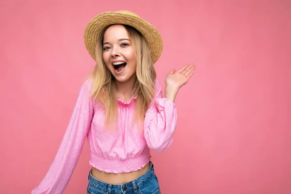 Portret van jonge aantrekkelijke glimlachende hipster blonde vrouw in stijlvolle roze gewas top en strohoed. Sexy zorgeloze vrouwelijke persoon poseren geïsoleerd in de buurt van roze muur in de studio. Positief model met natuurlijk — Stockfoto