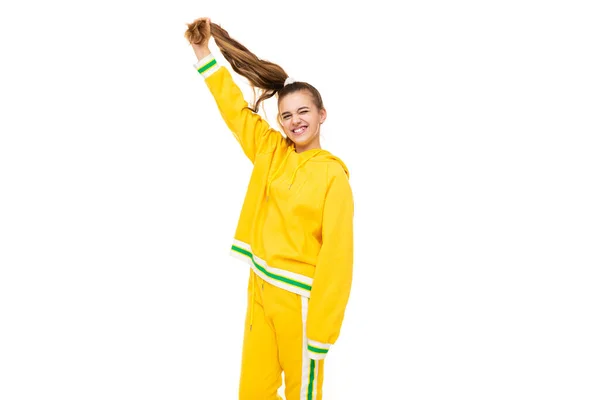 Φωτογραφία από το όμορφο αστείο χαρούμενο υπέροχο χαμογελαστό χαριτωμένο κορίτσι με σκούρα μαλλιά με αλογοουρά σε κομψό κίτρινο tracksuit με πράσινες ρίγες απομονώνονται σε λευκό φόντο με ελεύθερο χώρο για κείμενο — Φωτογραφία Αρχείου