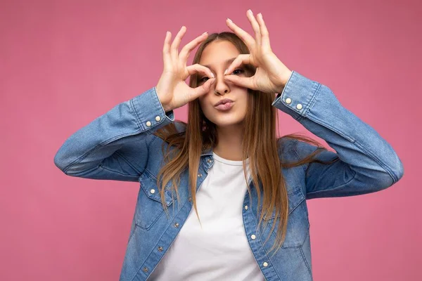 Mavi kot gömlek ve beyaz tişört giyen, samimi duyguları olan, neşeli, neşeli, genç, çekici, esmer bir kadının portresi. Pembe arka planda izole edilmiş, fotokopi alanı olan beyaz tişört.