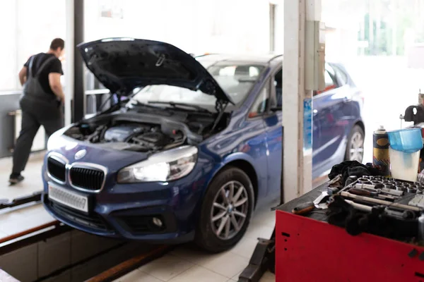 Photo of a blue passenger car at a service station under repair with an open hood and a mechanic — 图库照片