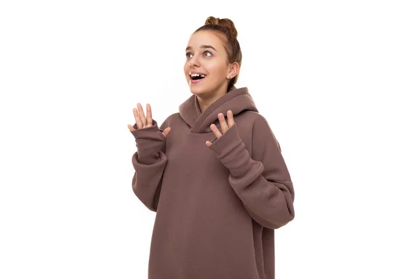 Photo of a beautiful cute girl with dark hair and a bun in a brown hoodie with a hood looks up in surprise isolated on a white background with free space for text — 图库照片