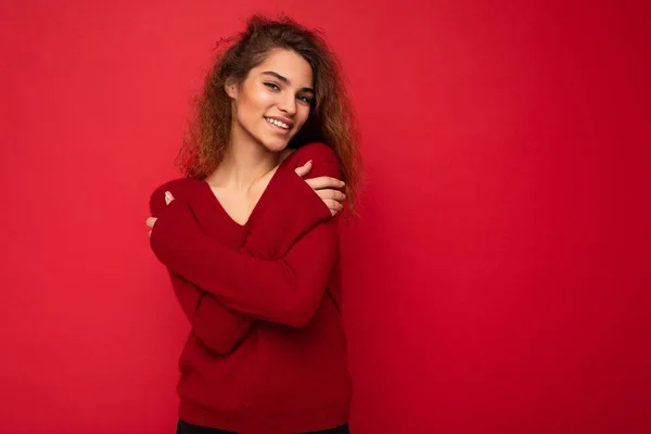 Fotografie krásné atraktivní pozitivní šťastný úsměv mladé brunetky kudrnaté žena na sobě stylový tmavě červený svetr izolované přes červené pozadí zeď s volným prostorem pro text — Stock fotografie
