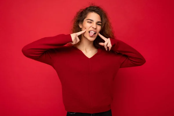 Φωτογραφία του νεαρού θετική ευτυχισμένη όμορφη μελαχρινή σγουρή γυναίκα με ειλικρινή συναισθήματα φορώντας casual κόκκινο πουλόβερ απομονώνονται σε κόκκινο φόντο με αντίγραφο χώρου και δείχνει απόχρωση — Φωτογραφία Αρχείου