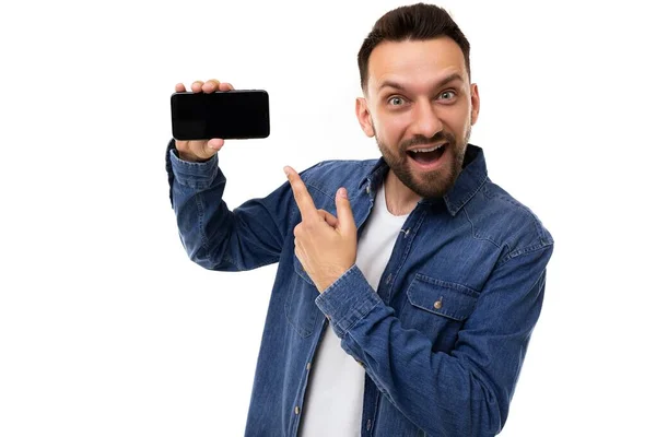 Jovem bonito aponta dedo na tela do smartphone com emoções carismáticas no rosto no fundo branco — Fotografia de Stock