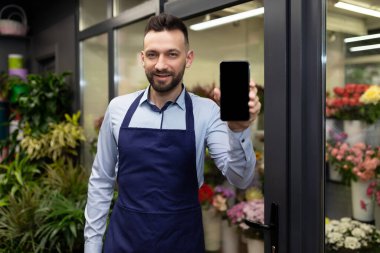 Çiçekler ve buketlerle buzdolabının yanındaki çiçekçi hayır diyor ve akıllı telefon ekranını gösteriyor.
