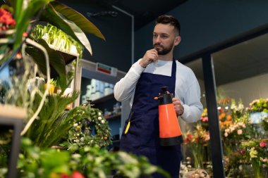 Çiçekçi dükkanındaki çiçekçi girişimci bitkilere su püskürtür.