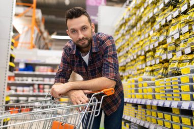 shopper in a hardware store looking at the camera bending over a trolley for goods, Concept of shopping for renovation and construction of a house