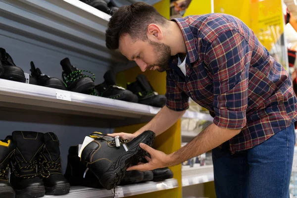 Man in a hardware store selects safety boots for work at a construction site, Concept of safety at a construction site — 스톡 사진