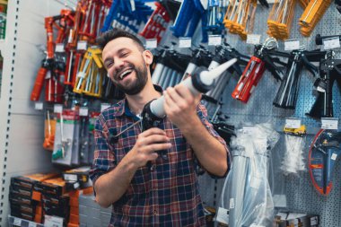 Yüzünde bir gülümseme olan hırdavatçıdaki bir müşteri yapıştırıcı macunu için silah seçiyor..