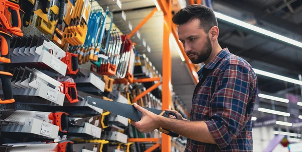 Acquirente maschio in un negozio di ferramenta sceglie un seghetto per legno. — Foto Stock