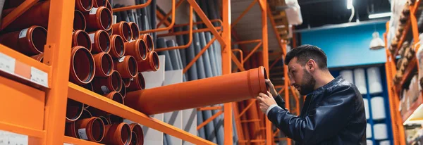 Een mannelijke koper in een ijzerwinkel kiest rioolbuizen voor sanitair werk — Stockfoto