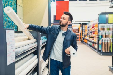 Hırdavatçıdaki bir müşteri duvarlar için duvar kağıdı seçer.