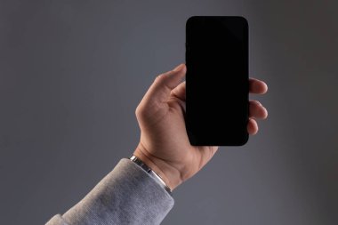 Gri arkaplanda erkek eli olan modern siyah akıllı telefon. Kopya alanı olan dikey telefon ekranı.