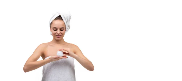 Young woman after a shower on a white background with a jar of white cream in her hands — Stock Photo, Image