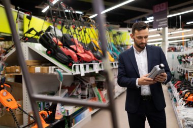 Mağazadaki bir müşteri benzin çim biçme makinesi için motor yağı seçiyor.