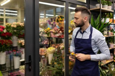 Elinde kahveyle bir çiçekçinin çalışanı. Buzdolabının arka planında buketler var.