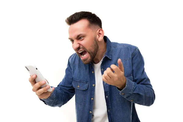 Homem zangado grita com a tela do telefone, gesticulando com as mãos com a boca aberta e franzindo a testa com as sobrancelhas, Conceito de raiva e agressão durante chamadas de vídeo — Fotografia de Stock