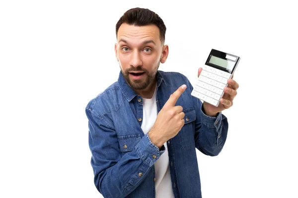 A serious middle-aged man with a beard showing a calculator screen pointing at it with his finger with his mouth parted indignantly — Stock Photo, Image