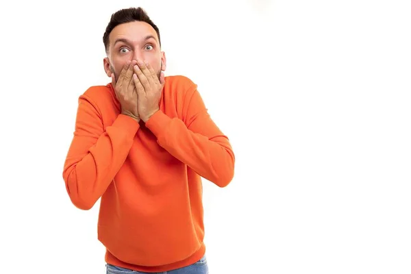 Überraschter und sprachloser Mann in orangefarbenem Pullover bedeckt entsetzt sein Gesicht mit den Handflächen — Stockfoto