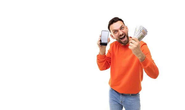 Человек с кучей денег в руках и экраном смартфона вперед счастливо машет руками, Концепция победителя в лотерее или пари — стоковое фото