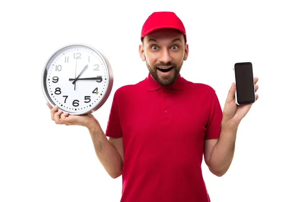 Kurier hält eine riesige Uhr in der Hand und zeigt den Bildschirm eines Smartphones in roter Uniform auf weißem Hintergrund — Stockfoto