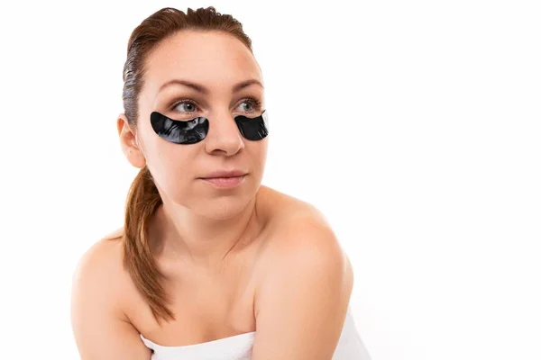 Young woman with black cosmetic patches under her eyes against a white wall — Stock Photo, Image