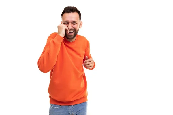 Un hombre en un suéter naranja se ríe sosteniendo sus manos en el estómago y la cara sobre un fondo blanco — Foto de Stock