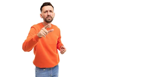 Чоловік на білому тлі в помаранчевому светрі вказує пальцем вперед вибираючи когось або щось збентежене — стокове фото