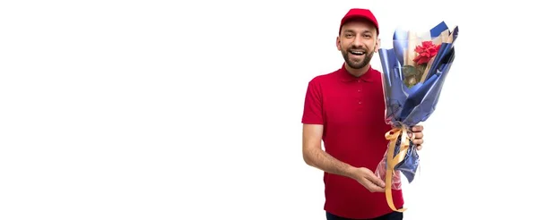 Mensajero en ropa roja con un magnífico ramo mirando a la cámara con una sonrisa sobre un fondo blanco — Foto de Stock