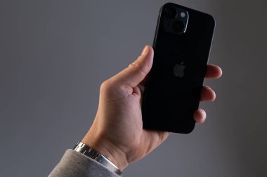 Gri bir duvara yaslanmış bir adam modern siyah bir iPhone 'u tutuyor. Elinde 13 akıllı telefon.