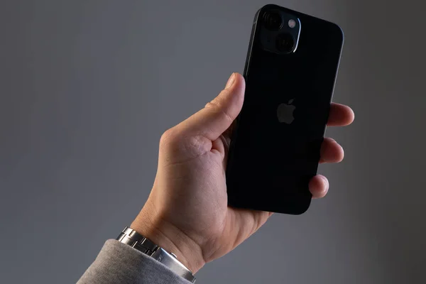 Een mans hand tegen een grijze muur houdt een moderne zwarte iPhone 13 smartphone in zijn handen — Stockfoto