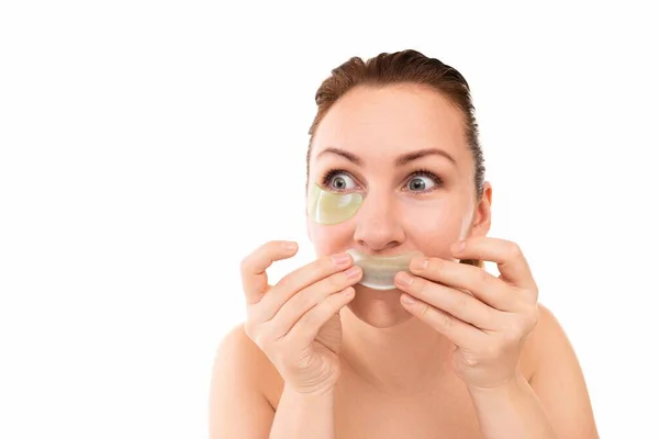 Young woman grimacing playfully lowers applying cosmetic patches under the eyes and on the lips — Stock Photo, Image
