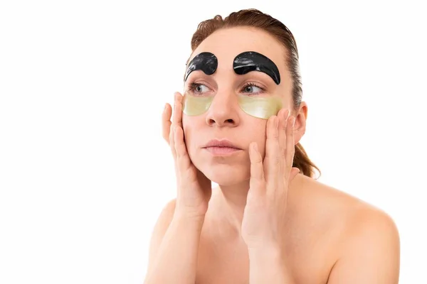 Seorang wanita merawat kulit wajahnya menggunakan kosmetik pada latar belakang putih yang terisolasi — Stok Foto