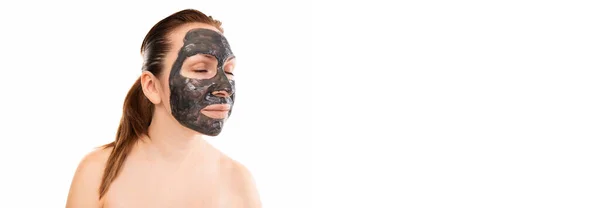 Retrato de uma mulher de meia-idade em uma máscara cosmética preta em seu rosto contra uma parede branca — Fotografia de Stock
