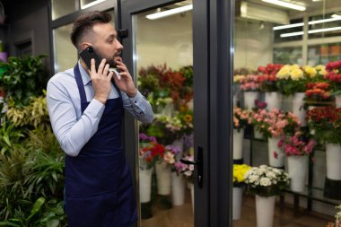 Çiçek merkezinin sahibi telefonda buzdolabının yanında buketlerle konuşuyor.