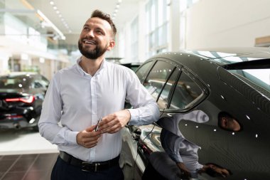 Araba galerisindeki bir adam yüzünde bir gülümsemeyle yeni bir araba hayal ediyor.