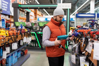 Elektrikli alet dükkanındaki erkek müşteri yeni bir elektrikli matkap seçiyor.