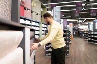 Bitiş malzemelerinden oluşan bir hırdavatçıda alıcı, ev ve apartman onarımı için vinil duvar kağıdı seçer