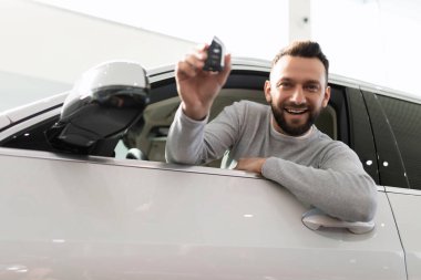 Tatmin olmuş bir müşteri elinde anahtarla arabadan dışarı bakar.