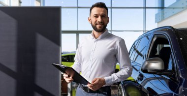 Yeni bir arabanın arka planına karşı elinde tabletle bir araba galerisi temsilcisi.